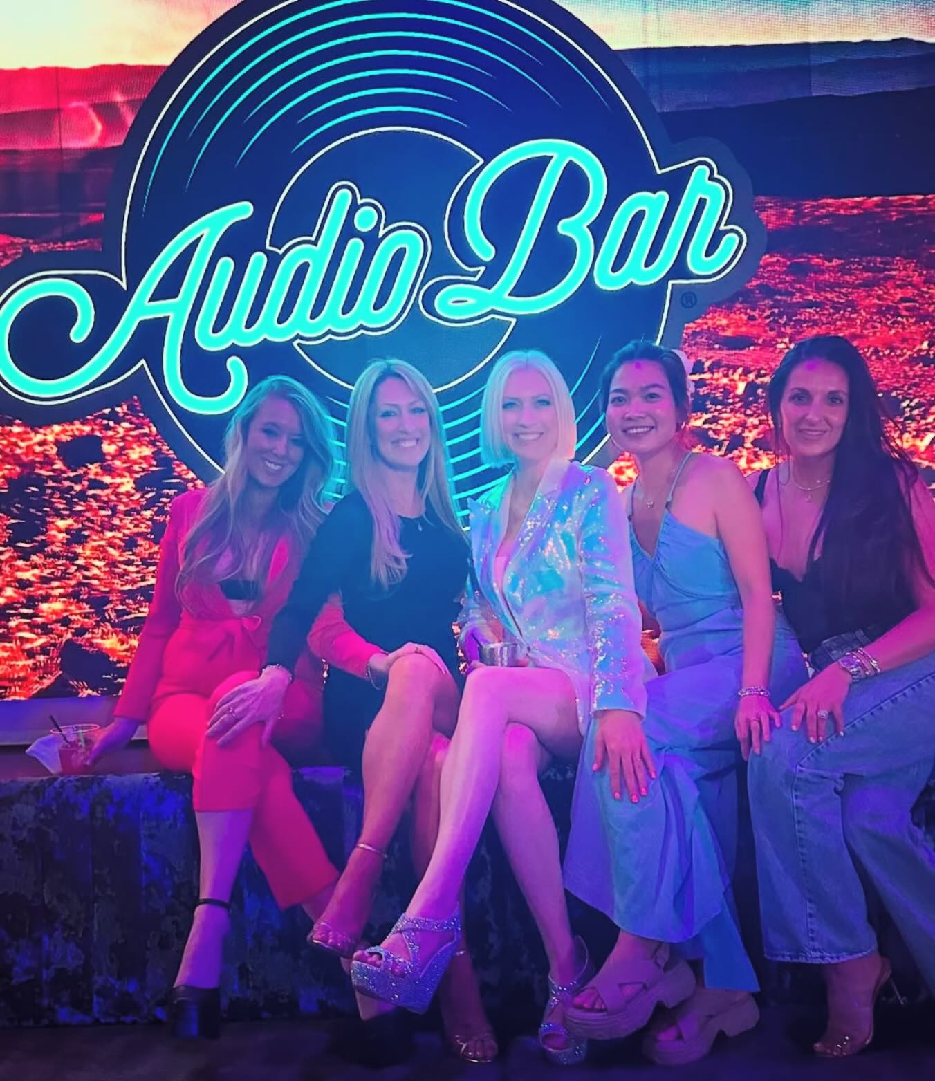 Guests posing in front of the Audio Bar neon sign